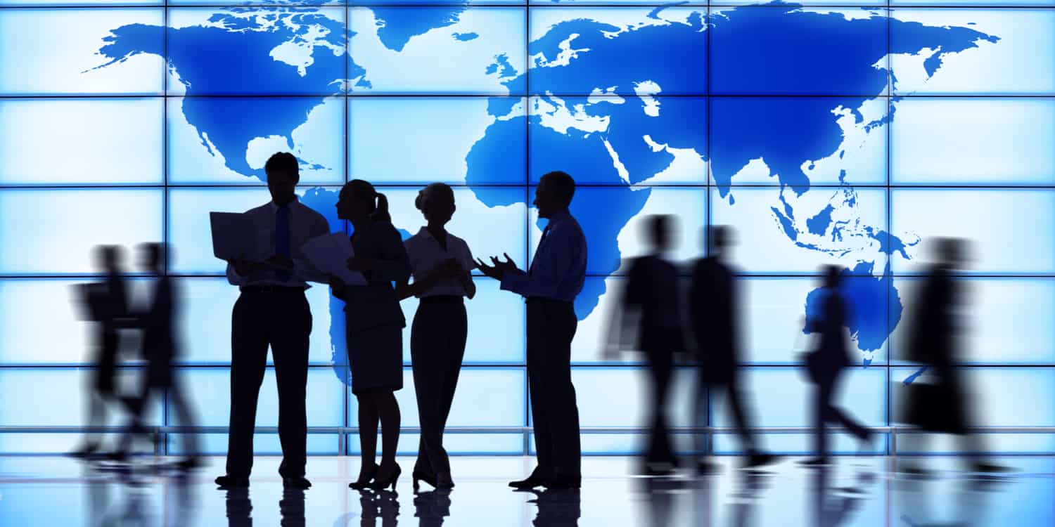 Business people silhouetted against a large glass wall displaying a map of the world.