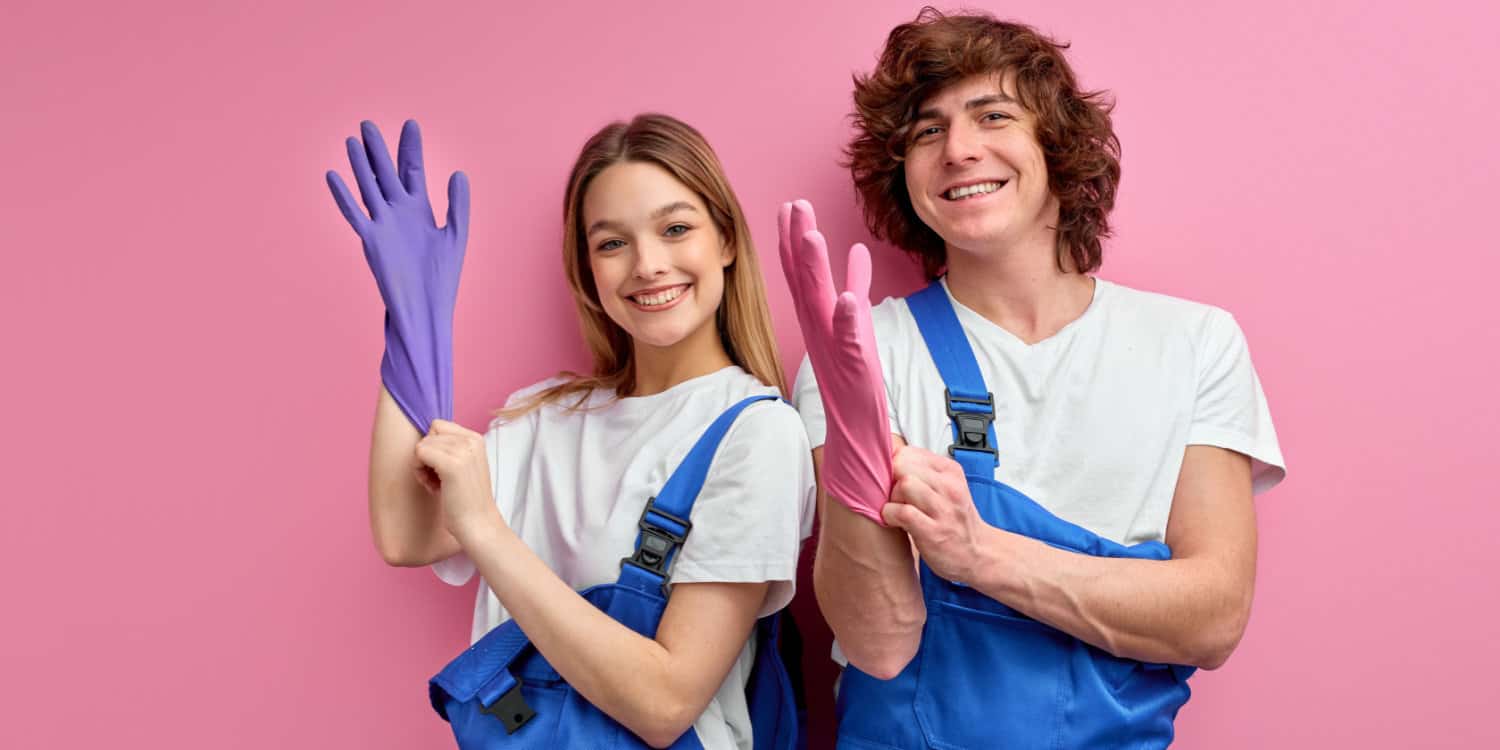 Happy cleaning business owners in overalls wearing rubber gloves preparing for cleaning, with pink studio background