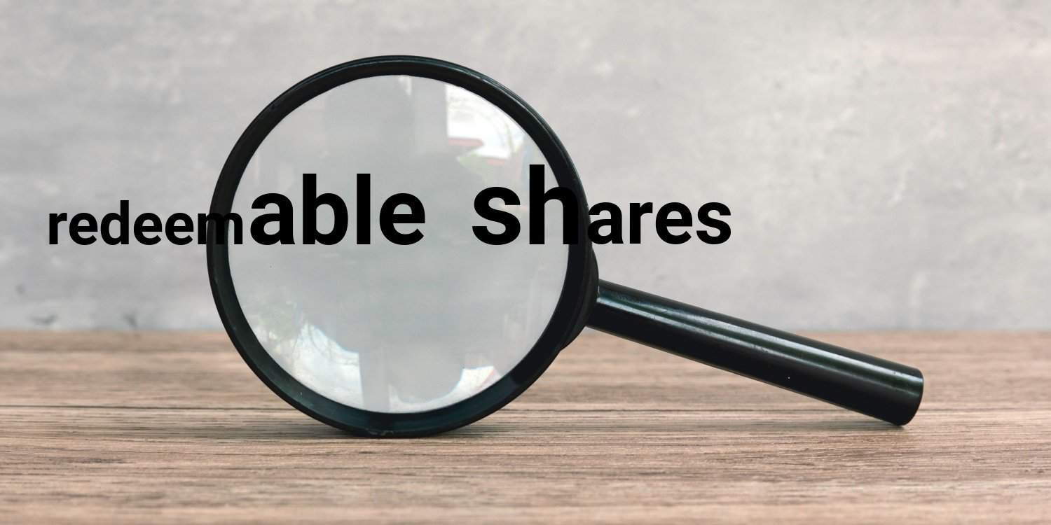 Magnifying glass sitting on a wooden desk with the words 'redeemable shares'.